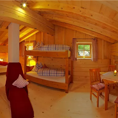 Ein gemütlicher Raum mit Holzverkleidung, Doppelbett und Etagenbetten. Ein kleiner Tisch mit Stühlen rundet die Einrichtung ab.