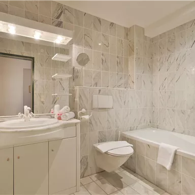 Ein modernes Badezimmer mit Marmorfliesen, einer Badewanne und einem Waschbecken. Eine helle Beleuchtung sorgt für eine einladende Atmosphäre.