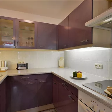 Eine moderne Küche mit dunklen Schränken und hellen Arbeitsflächen. Auf der Arbeitsplatte liegen frische Lebensmittel und Kochutensilien.