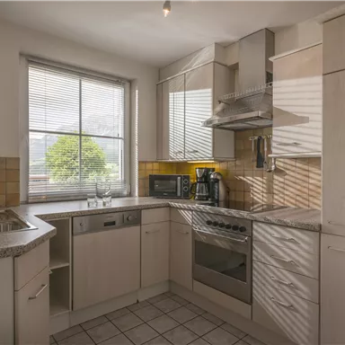 Eine moderne Küche mit hellen Möbeln und einem großen Fenster. Die Geräte sind gut ausgestattet und es gibt viel Platz zum Kochen.