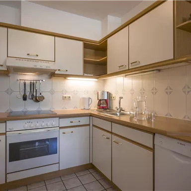 Eine moderne Küche mit hellen Schränken und einer klaren Arbeitsfläche. Sie ist gut ausgestattet mit Geräten wie Herd und Geschirrspüler.