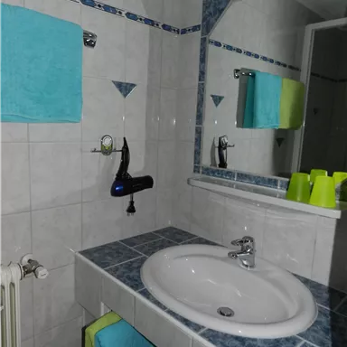 Ein modernes Badezimmer mit einem Waschbecken und einem großen Spiegel. Bunte Handtücher hängen an der Wand, und auf dem Waschbecken steht eine grüne Flasche.