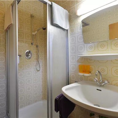 A modern bathroom with a shower and a sink. The walls are decorated with a classic patterned wallpaper.