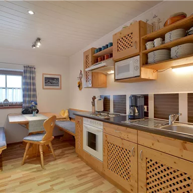 Eine gemütliche Küchenzeile mit Holzschränken und moderner Ausstattung. Es gibt einen kleinen Essbereich mit einer Sitzbank und einem Tisch.