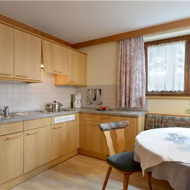 A cozy kitchen with wooden-clad cabinets and a small dining area. On the table, there is a wine and fresh flowers.
