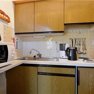 A bright kitchen with wooden cabinets and modern appliances. There is a microwave, a kettle, and cooking utensils.
