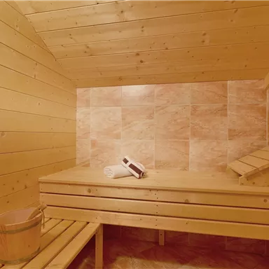 Eine gemütliche Sauna mit Holzverkleidung und benutzbarem Ruhebett. Auf der Bank liegen ein Handtuch und eine Saunakelle.