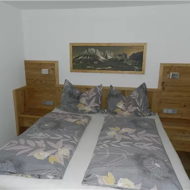 Ein gemütliches Schlafzimmer mit einem Doppelbett und stilvollen Holzmöbeln. Die Wände sind in neutralen Farben gehalten, und ein Bild von Bergen schmückt die Wand.