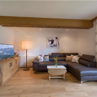 A modern living room with a cozy couch and a television. The room is bright and inviting, with wood and textile decorations.