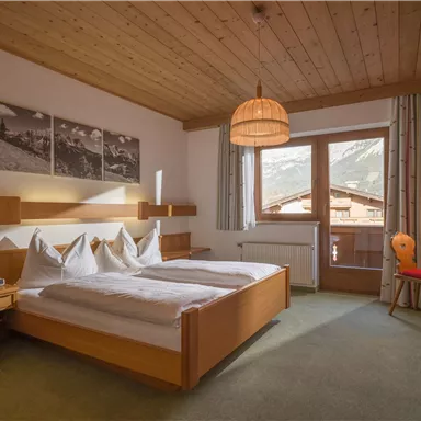 Ein helles Hotelzimmer mit einem Doppelbett und modernen Möbeln. Die großen Fenster bieten einen Blick auf die Berge und sorgen für eine angenehme Atmosphäre.