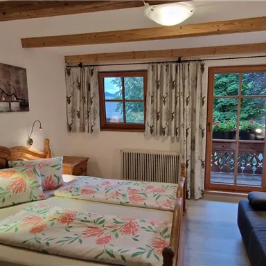 Ein gemütliches Schlafzimmer mit zwei Betten und einem Sofa. Große Fenster erlauben einen Blick ins Grüne.