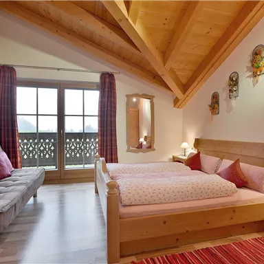 Ein gemütliches Schlafzimmer mit Holzdecke und großen Fenstern. Das Zimmer ist hell und freundlich eingerichtet, mit einem Doppelbett und einem Schlafsofa.