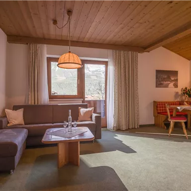 Ein gemütliches Wohnzimmer mit Holzdecke, einem Sofa und einem Tisch. Große Fenster sorgen für viel Tageslicht und der Essbereich lädt zum Verweilen ein.