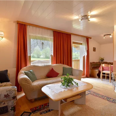 Ein gemütliches Wohnzimmer mit bequemen Sofas und einem niedrigen Tisch. Große Fenster lassen viel Licht herein und schaffen eine einladende Atmosphäre.