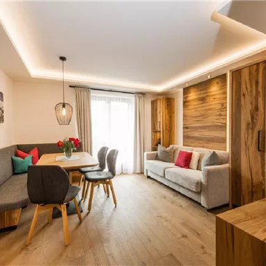 A modern living room with a stylish dining table and cozy seating. Large windows provide plenty of daylight and a warm atmosphere.