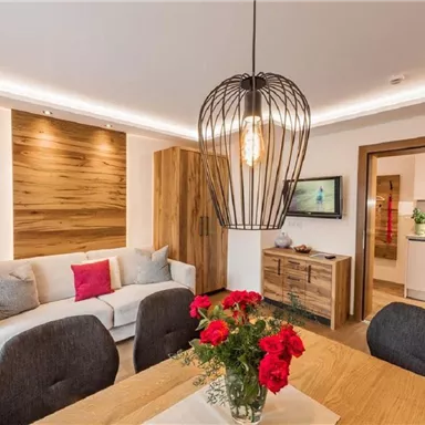 A modern living room with a cozy couch and a wooden table. A large chandelier and fresh flowers create an inviting atmosphere.