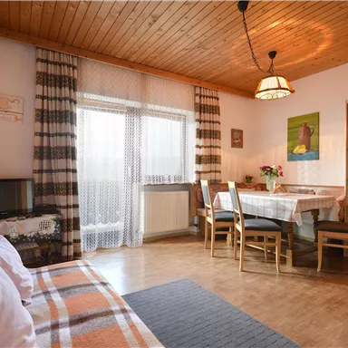 A cozy living room with a wooden ceiling and a dining area. Large windows provide plenty of daylight and an inviting atmosphere.