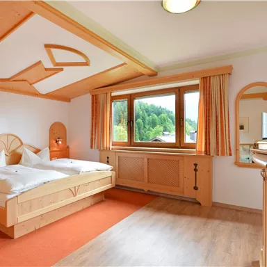 Ein gemütliches Schlafzimmer mit einem großen Bett und Holzdetails. Es gibt ein Fenster mit Blick auf die Natur und einen Fernseher im Raum.