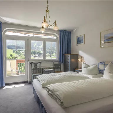 Ein gemütliches Schlafzimmer mit zwei Betten und einem großen Fenster. Der Raum hat blaue Vorhänge und einen Blick auf die Landschaft.