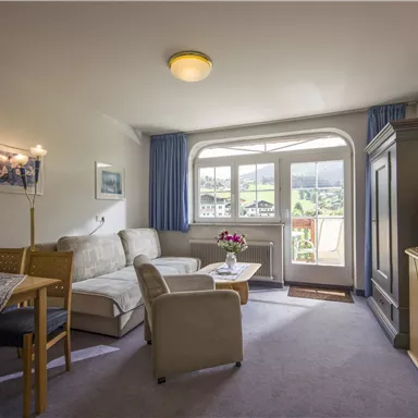 Ein helles Wohnzimmer mit einem gemütlichen Sofa und einem Tisch. Große Fenster bieten einen schönen Blick nach draußen.