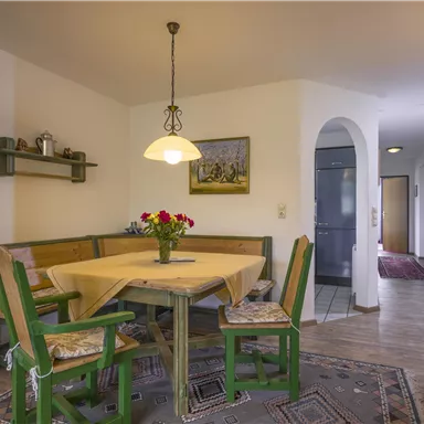 Eine gemütliche Essküche mit einem Holztisch und bunten Stühlen. Ein Blumenstrauß in der Mitte des Tisches sorgt für eine freundliche Atmosphäre.