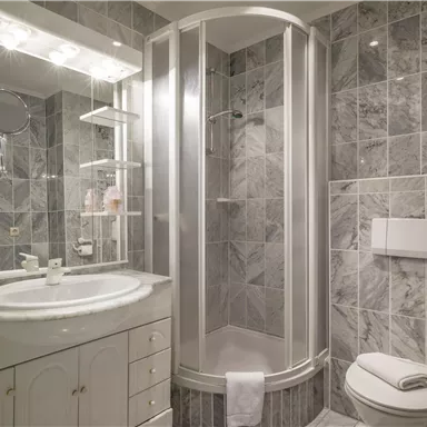 Ein modernes Badezimmer mit marmorierten Wänden. Es enthält eine Dusche, ein Waschbecken und eine Toilette.