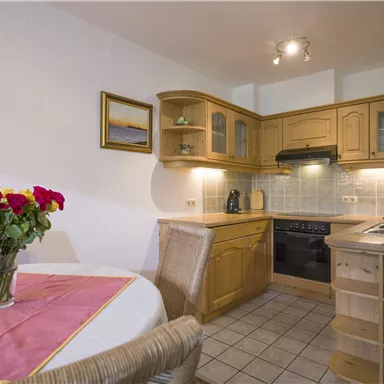 Eine helle Küche mit Holzschränken und modernem Equipment. Auf dem Tisch steht eine Vase mit roten Rosen.