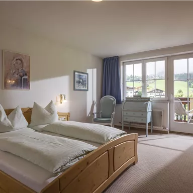 Ein gemütliches Schlafzimmer mit einem großen Doppelbett, zwei Kissen und einem Schreibtisch. Große Fenster bieten einen Blick auf die schöne Landschaft draußen.