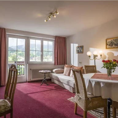 Ein gemütlicher Wohnraum mit einem Esstisch, einer Couch und einem Fernseher. Große Fenster bieten einen Blick auf die Landschaft.