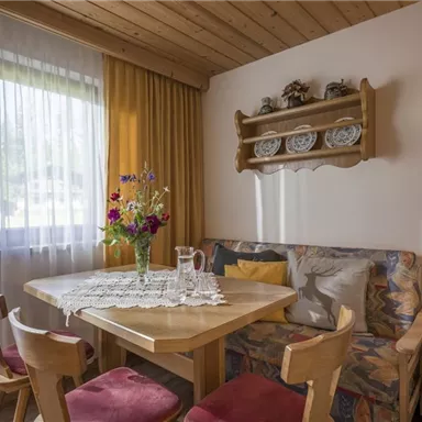 Ein gemütlicher Essbereich mit einem Holztisch und Stühlen. Auf dem Tisch steht eine Blumenvase und der Raum ist hell und freundlich gestaltet.