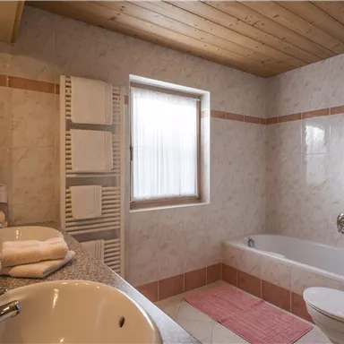 Ein modernes Badezimmer mit einer Badewanne, zwei Waschbecken und Holzdecke. Es gibt auch Handtücher und eine Heizung im Raum.