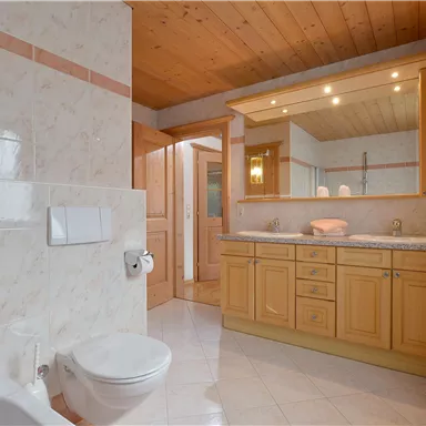 Ein modernes Badezimmer mit Holzdecke und hellen Fliesen. Es gibt eine Dusche, eine Toilette und einen großen Spiegel über dem Waschbecken.