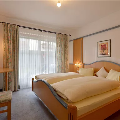 Ein gemütliches Schlafzimmer mit zwei Betten und weichen Kissen. Große Fenster sorgen für viel Tageslicht und die Einrichtung ist modern und einladend.