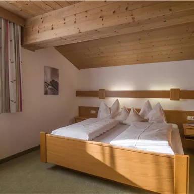 Ein gemütliches Schlafzimmer mit Holzdecke und zwei Einzelbetten. Der Raum ist hell und freundlich mit einem Fenster und modernem Mobiliar.