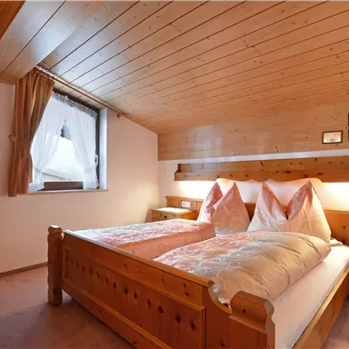 Ein gemütliches Schlafzimmer mit holzverkleideten Wänden und einem Doppelbett. Die Fenster lassen natürliches Licht herein und schaffen eine warme Atmosphäre.