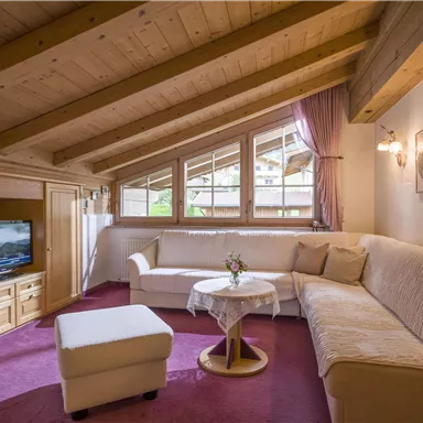 Ein gemütlicher Wohnraum im Dachgeschoss mit einer hellen Sitzecke. Große Fenster sorgen für viel Tageslicht und eine warme Atmosphäre.