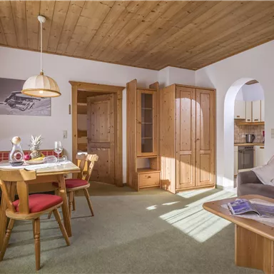 Ein gemütlicher Wohnraum mit einem Esstisch und vier Stühlen. Die Einrichtung ist hell und einladend, mit einem Holzdecke und einer kleinen Küchenzeile im Hintergrund.