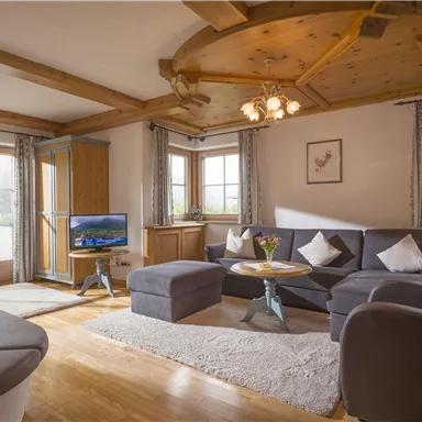 Ein gemütliches Wohnzimmer mit einem komfortablen Sofa und einem kleinen Tisch. Große Fenster lassen viel Tageslicht herein und bieten einen Blick nach draußen.