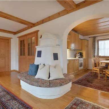 Ein gemütliches Wohnzimmer mit Holzbalkendecke und einem hellen Essbereich. Der Raum ist gut beleuchtet und bietet eine einladende Atmosphäre.