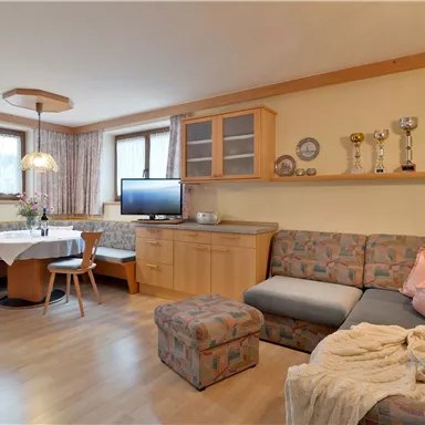 A cozy living space with a couch, a table, and chairs. Several trophies are displayed on the wall, and the lighting is pleasant.