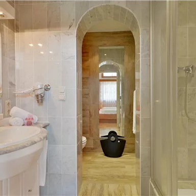 Ein modernes Badezimmer mit hellen Fliesen und einem Waschbecken. Im Hintergrund ist ein angelegter Bereich mit einem Schlafzimmer sichtbar.