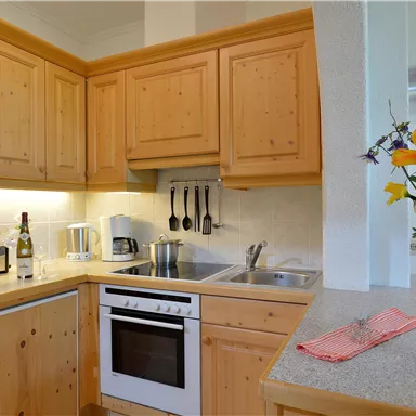 Eine gemütliche Küche mit Holzschränken und moderner Ausstattung. Auf der Arbeitsplatte steht eine Vase mit bunten Blumen.