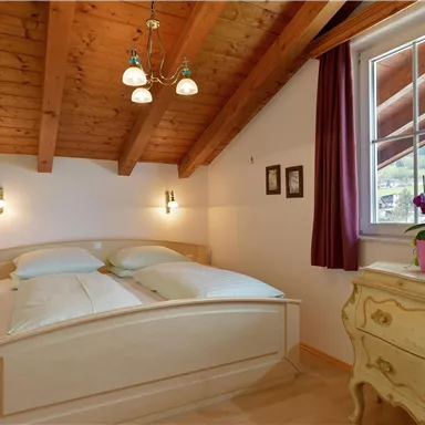 Ein gemütliches Schlafzimmer mit Holzdecke und großen Fenstern. Es enthält ein Doppelbett, einen Nachttisch und eine Kommode.