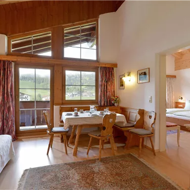 Ein gemütliches Wohnzimmer mit einem Tisch, Stühlen und einem Sofa. Große Fenster bieten einen Blick auf die umliegende Natur.