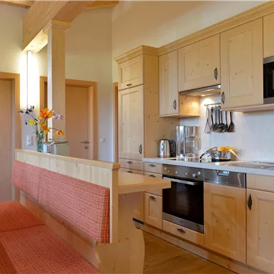 Eine moderne Küche mit Holzmöbeln und einer einladenden Sitzecke. Die Ausstattung umfasst einen Herd, eine Mikrowelle und Küchenutensilien.