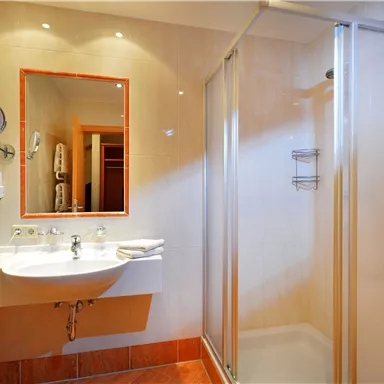 A modern bathroom with a shower and a sink. The walls are bright, and the room feels clean and inviting.
