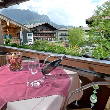 Ein schöner Tisch auf einer Terrasse mit Blick auf die Berge. Auf dem Tisch stehen ein Flasche Sekt und Gläser, umgeben von bunten Blumen.