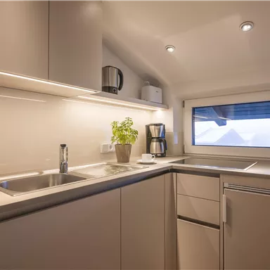 A modern kitchen with bright cabinets and a large window front. On the countertop, there is a coffee machine and a plant.