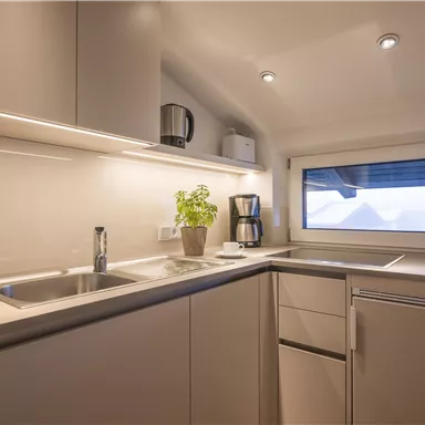 A modern kitchen with bright cabinets and a large window front. On the countertop, there is a coffee machine and a plant.