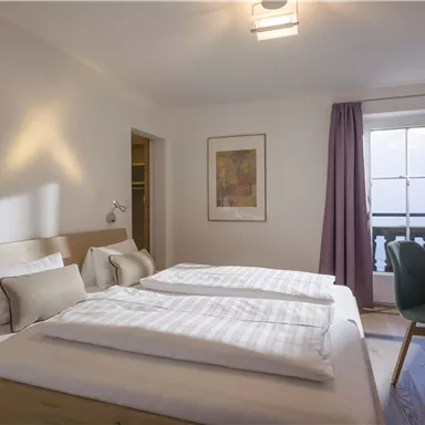 A bright and modern bedroom with two single beds. There is a desk, a television, and a window with curtains.